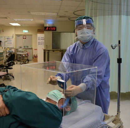 Doctor sosteniendo una caja acrílica de bioseguridad sobre un paciente.